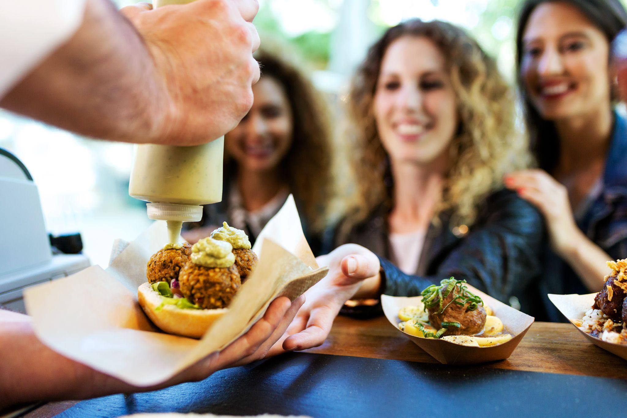 Three beautiful young women buying meatballs on a food truck.