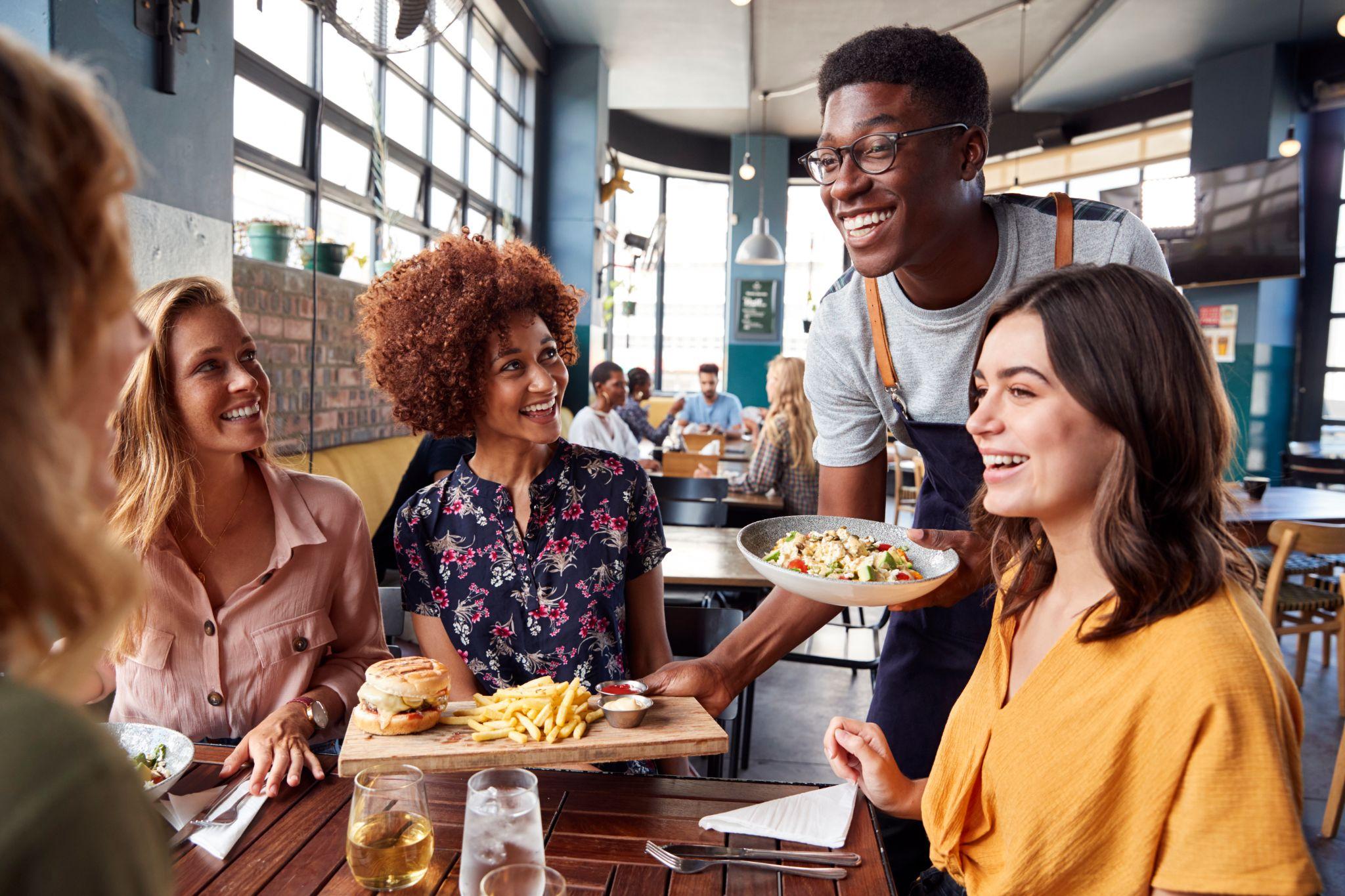 waiter-serving-group-of-female-friends-meeting-for-drinks-and-food-in-restaurant