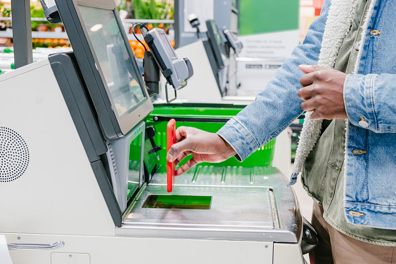 Man using smartphone at self checkout at convenience store.